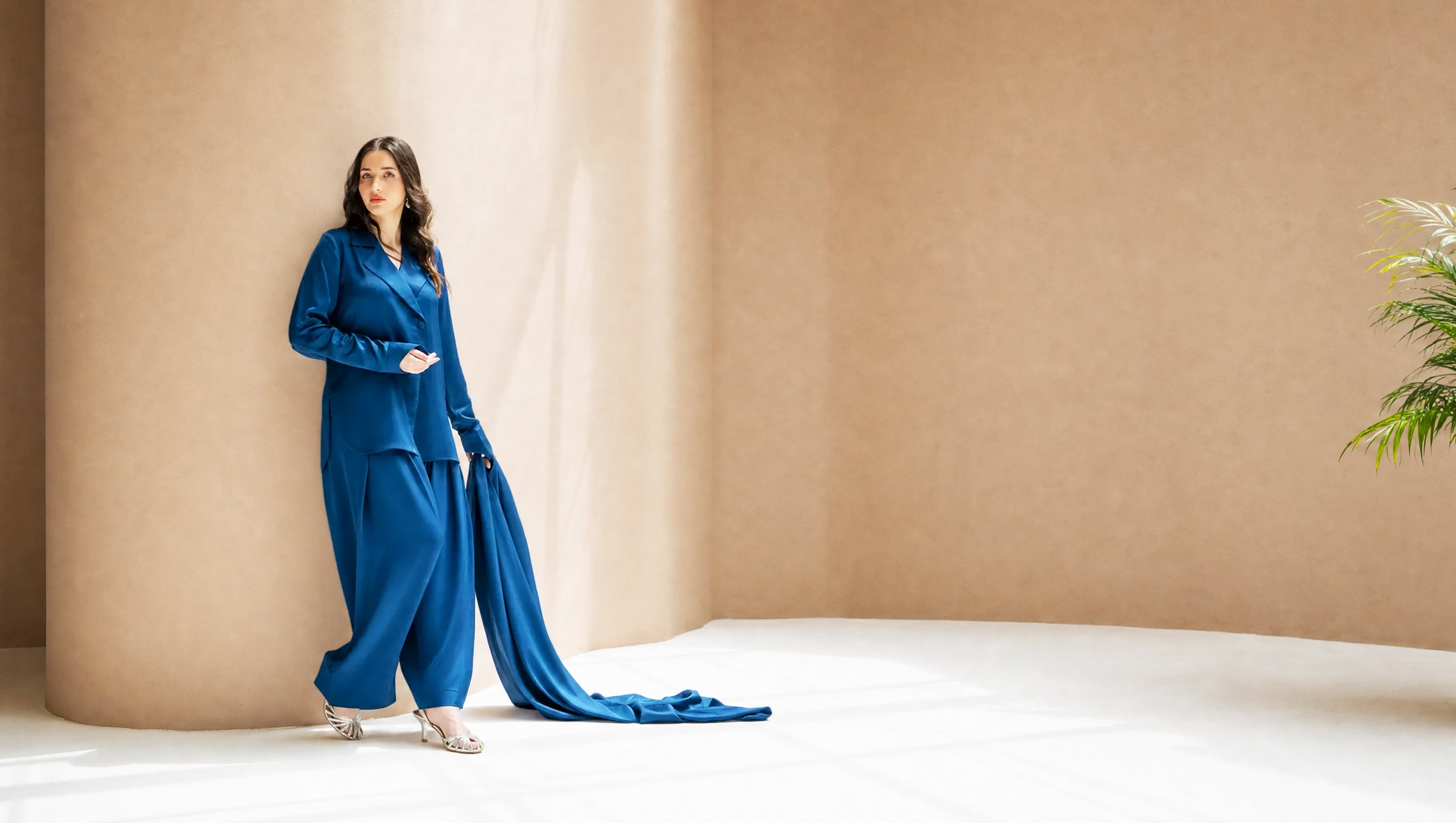 Woman in a blue outfit standing in a minimalistic room with beige walls and a white floor.